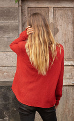 Load image into Gallery viewer, Back top half view of a woman wearing jeans and the wooden ships mini reindeer crew sweater. This sweater is poppy red colored with long sleeves.
