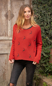 Front top half view of a woman wearing jeans and the wooden ships mini reindeer crew sweater. This sweater is poppy colored with a mini reindeer print on the front in the color ink. This sweater has long sleeves and a crew neck.