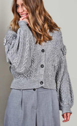 Load image into Gallery viewer, Front top half view of a woman wearing the summum balloon sleeve cardigan in the color fog/grey. This sweater has a cable knit pattern, a button down front, and fringe on the balloon sleeves.
