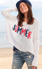Load image into Gallery viewer, front top half view of a woman on a beach wearing the wooden ships summer loving crew top and jean shorts. This knit top is white with the word summer knit into the front center of it in red and blue. The top has a boxy silhouette and long sleeves.
