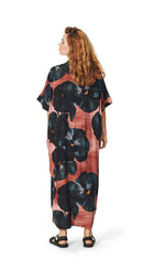 Load image into Gallery viewer, Back full body view of a woman wearing the bitte kai rand black hibiscus long dress. This dress is pink with large black hibiscus flowers all over it. The dress has elbow-length sleeves, a v-neck, and a hem that sits at the ankles.
