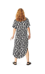 Back full body view of a woman wearing the Bitte Kai Rand Graphic Leaves Long Dress. This dress features a black and white leaf print all over it. It has short sleeves and a rounded hem.