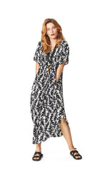 Load image into Gallery viewer, Front full body view of a woman wearing the Bitte Kai Rand Graphic Leaves Long Dress. This dress features a black and white leaf print all over it. It has short sleeves, a v-neck, and a rounded hem.
