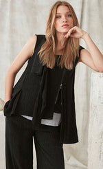 Load image into Gallery viewer, Front top half view of a woman wearing the crea concept black vest/top. This top is sleeveless with a draped front, a zipper on the front left side, and an asymmetrical hem.
