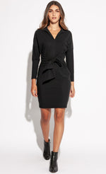 Load image into Gallery viewer, Front full body view of a woman walking forward wearing the Indies Irina Dress. This black fitted dress cuts off above the knees and has long sleeves and a large tie belt on the waist.
