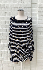 Front view of a mannequin wearing the Frank Lyman Navy & White Striped Knit Tunic. This striped tunic features gold dots all over it, 3/4 length dolman sleeves, and a gathering on the left side near the hip.