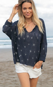Front top half view of a woman on the beach wearing white shorts and the wooden ships mini starfish top in indigo. This top has 3/4 length sleeves, a v-neck and an oversized silhouette.