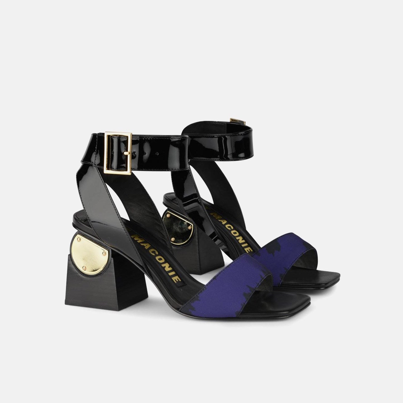 Outer and inner side view of a pair of the kat maconie nyla sandal. This sandal has a black patent leather upper near the heel and a black patent leather ankle strap with a buckle. The upper near the square toe is blue and varnished. The heel is black with a gold circle.