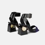 Load image into Gallery viewer, Back view of the kat maconie nyla sandal. This sandal has a black patent leather upper near the heel and a black patent leather ankle strap with a buckle. The upper near the square toe is blue and varnished. The heel is black with a gold circle.
