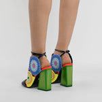 Load image into Gallery viewer, Back view of a woman wearing a pair of the kat maconie frida glitch high heel. This shoe features bright mutlicolored circles on the upper with a black strap over the toes and a black ankle strap. The high heel is green.
