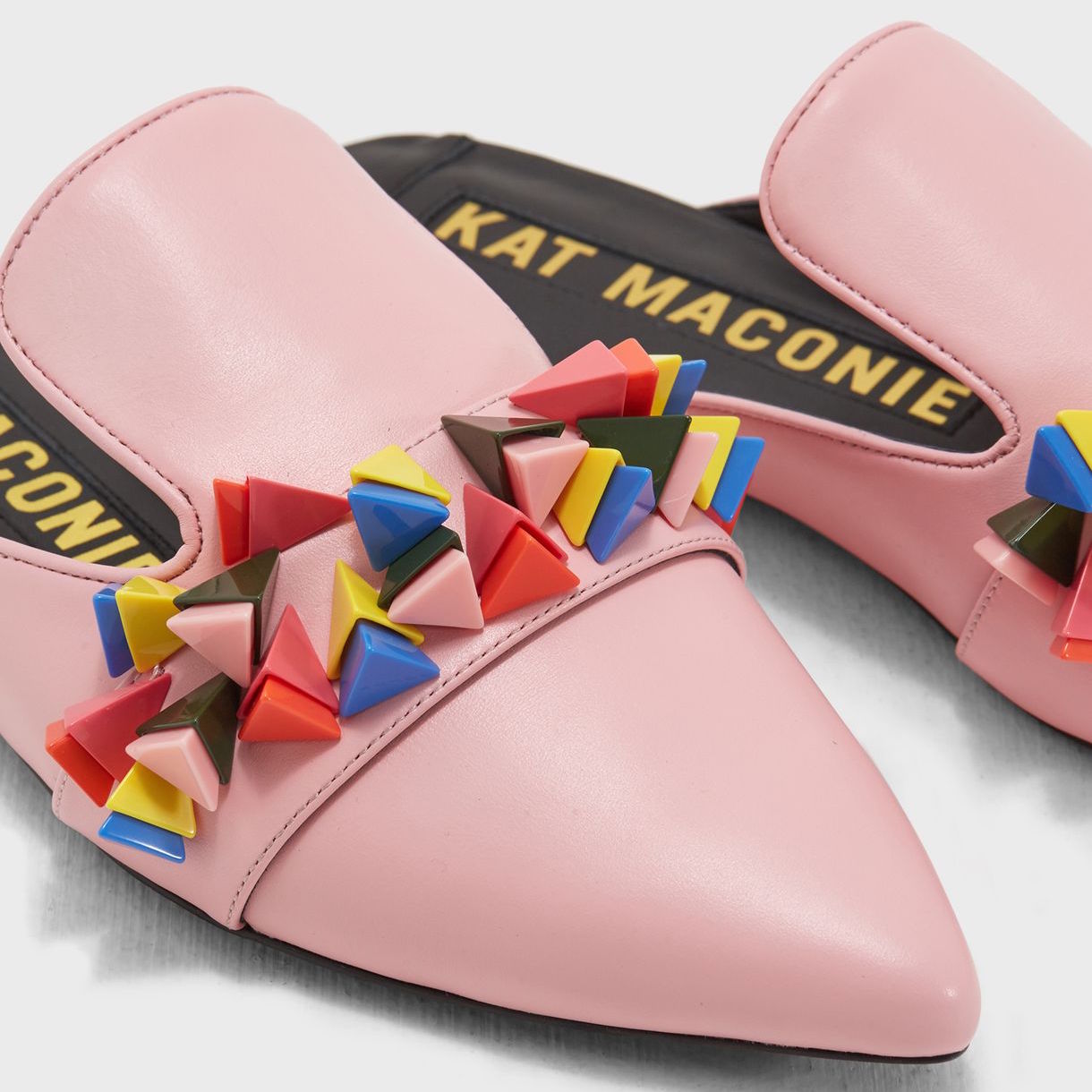 Close up view of a pair of the kat maconie issa mule. This slip on mule is pink with multicolored tiny pyramid shaped decorations on the upper. The shoe has a pointed toe.