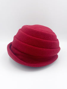 Left side view of the lillie & cohoe beatrice hat. This hat is red with a tiered/folded crown and a rounded brim.