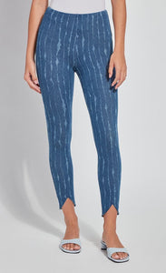 Front bottom half view of a woman wearing the lysse lynette scallop edge denim pattern legging. The leggings are a mid-wash denim color with white streaks running vertically down the leg. The pants are high-waisted and have a tulip shaped cut at the hem near the ankles. 